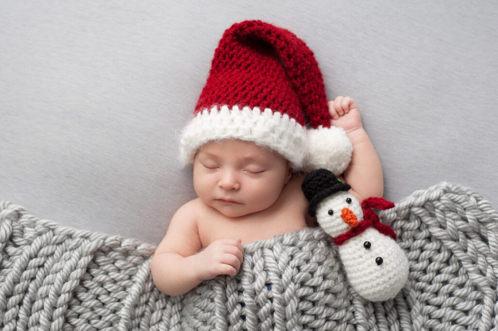 a baby sleeping in a red and white hat with a snowman toy