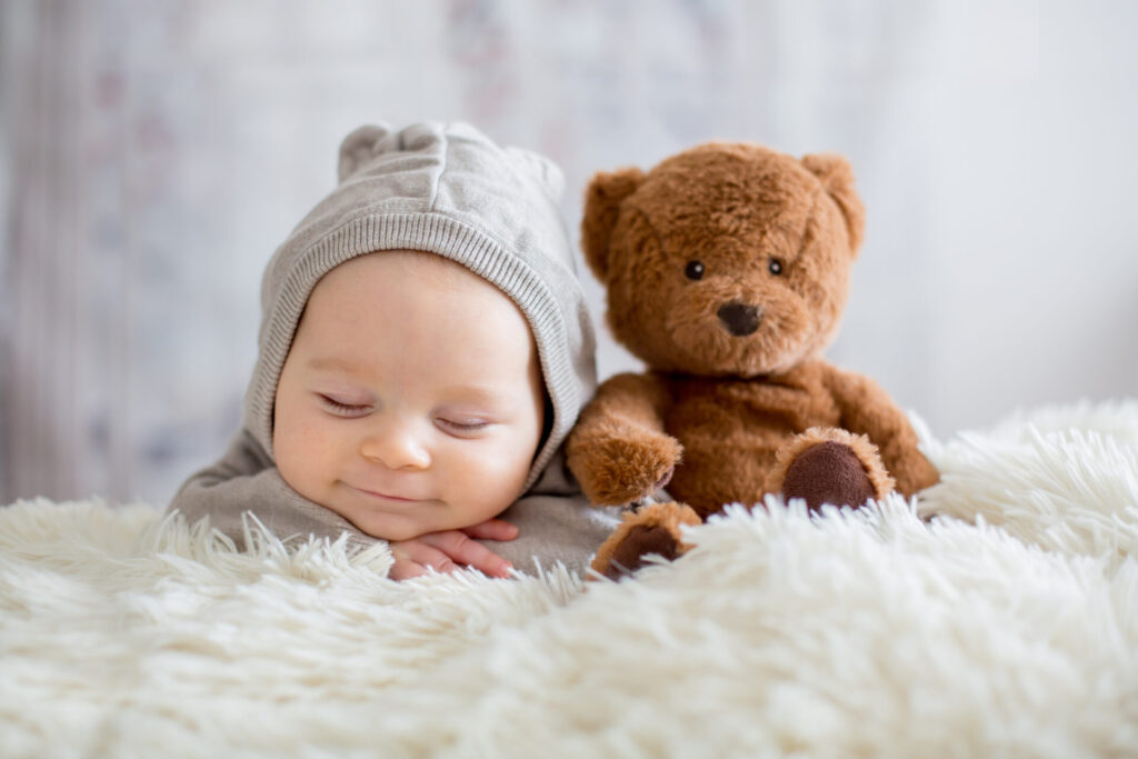 a baby lying next to a stuffed bear